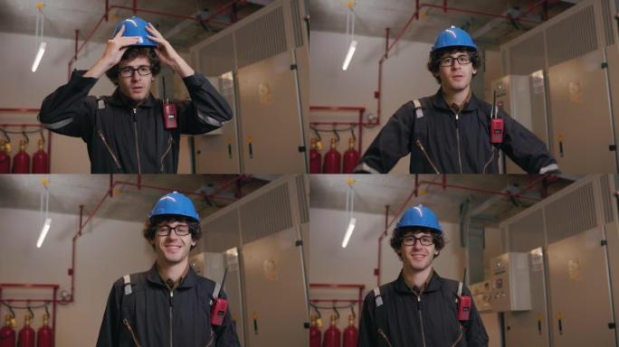 在仓库工厂工作的年轻专业工程师。穿着安全制服和安全帽的工程师。技术人员站在电气柜控制附近看着摄像机。