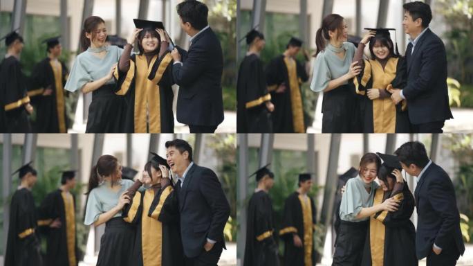 自豪的亚洲华裔父母在大学大楼外的大学毕业礼服中调整女儿的迫击炮