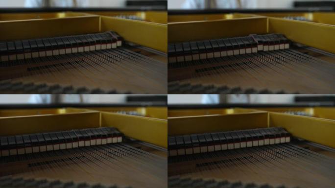 在大钢琴琴弦上敲打着柔软的锤子的极端特写镜头，而无法辨认的女钢琴家则在模糊的背景上演奏。