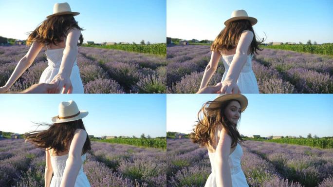 戴着帽子的漂亮女人握着男性的手，在薰衣草田里慢跑。幸福的情侣在花草地上玩得开心。穿着裙子跑的女孩回头