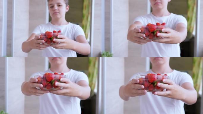 孩子手里拿着满玻璃碗红色的草莓在阳光下在房间里