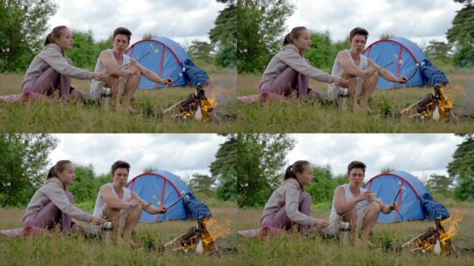 年轻夫妇坐在篝火旁煮棉花糖的草地上