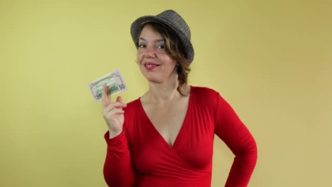 一个穿着红色毛衣和帽子的女人在孤立的黄色背景上显示五十美元