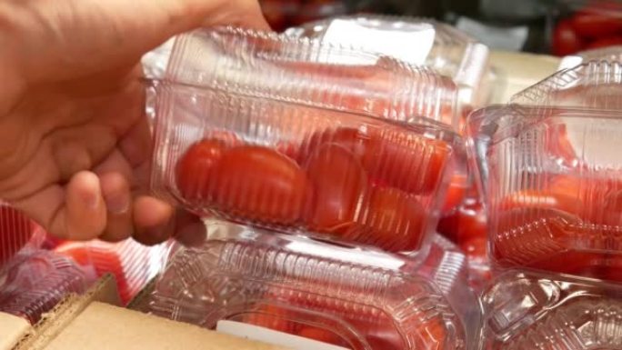 许多装有红色西红柿的塑料盒和一个男性买家的手拿一个