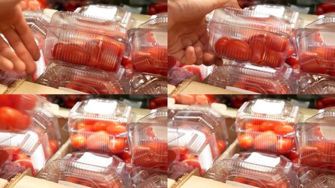 许多装有红色西红柿的塑料盒和一个男性买家的手拿一个