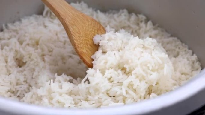 用饭勺从锅里舀米饭，用木勺在锅里煮米饭