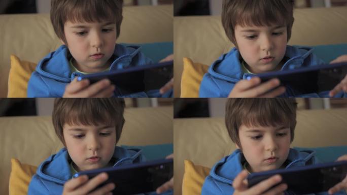 孩子坐在沙发上玩手机游戏。男孩用手机玩电子游戏。学龄前儿童在沙发上玩电子游戏。孩子用手机玩在线教育社