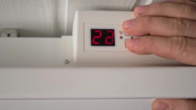 男子降低电加热器的温度。特写。由于供暖成本价格上涨，调节散热器上的恒温器以节省能源。节能。摄氏单位。