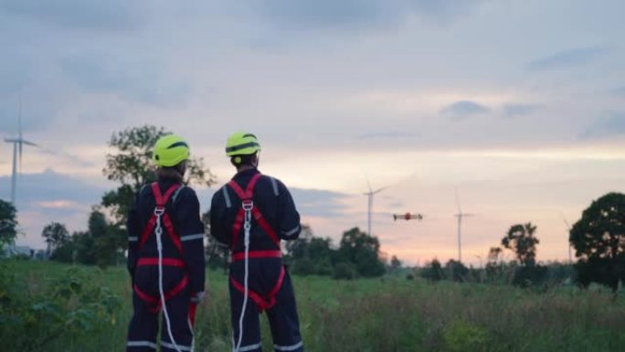 两名亚洲技术人员穿着安全套，驾驶无人机检查风力涡轮机的运行情况。