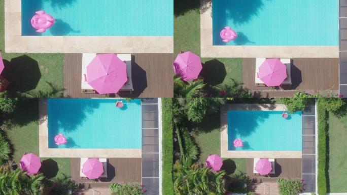 空中自上而下的镜头显示后院的游泳池，空中无人机上升镜头，粉红色的雨伞，粉红色的火烈鸟浮标