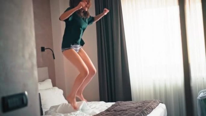 一个年轻的高加索人兴奋的女人在床上跳跃和跳舞