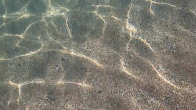 太阳的眩光反映在最纯净的透明海水特写，沙质海底。由于微风，小浪冲入水中。