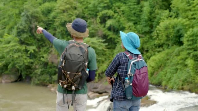 4K，喜欢在森林中旅行和爬山的亚洲男女游客站在瀑布悬崖的边缘，欣赏美丽的大自然和森林的水分