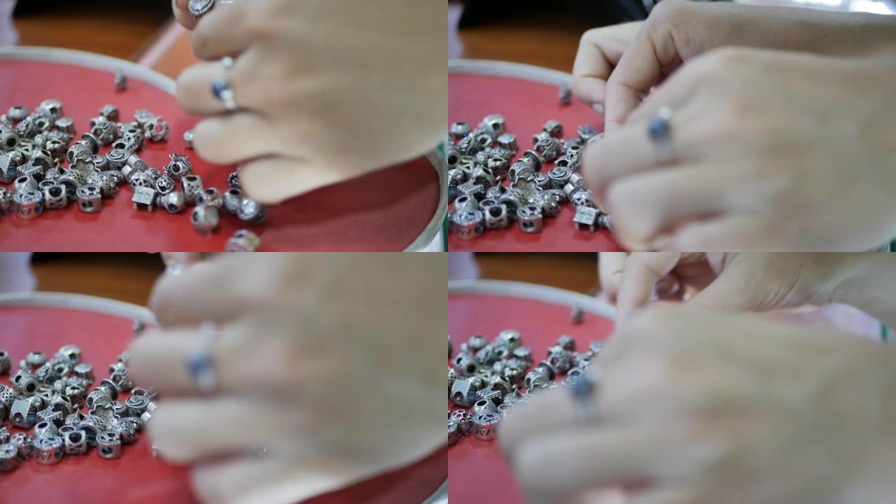女人的手从一堆银饰中挑选，用手指按出数字和符号形式的手镯上的银链