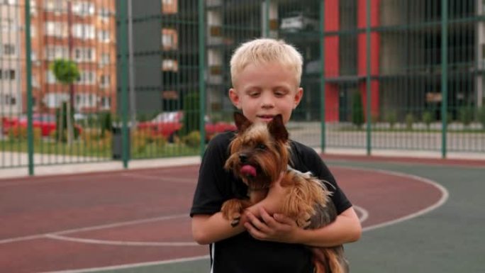 一个男孩抱着约克夏犬站在院子里的运动场上。