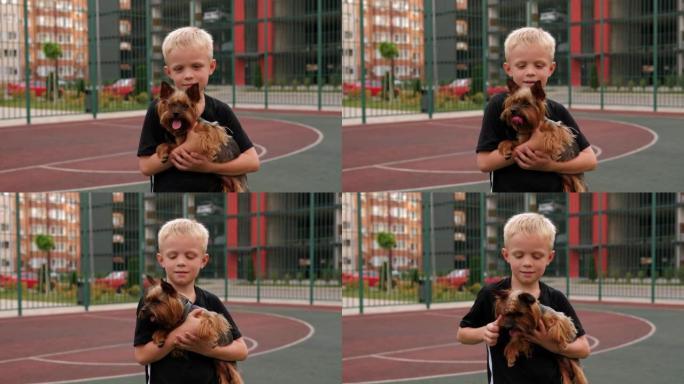 一个男孩抱着约克夏犬站在院子里的运动场上。