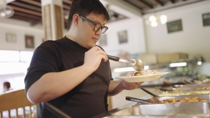 大型建筑男子从自助餐托盘中选择食物。