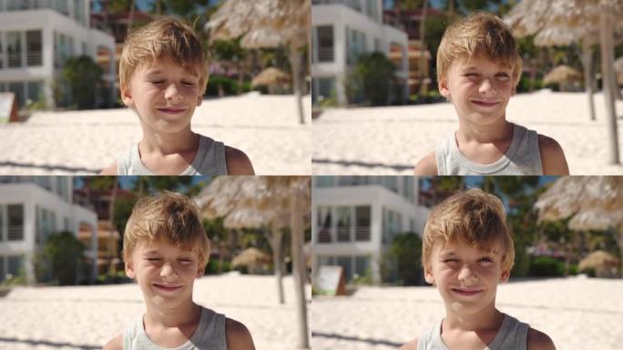 海滩上一个年轻的白人金发男孩的肖像。他眯着眼睛看着太阳，看着相机