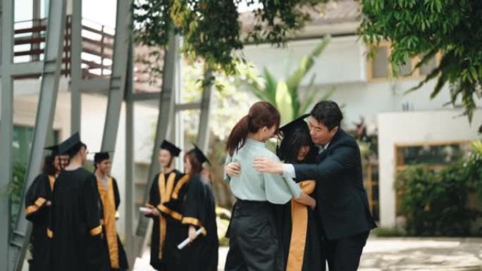 自豪的亚洲华裔父母带着女儿在大学大楼外的大学毕业礼服
