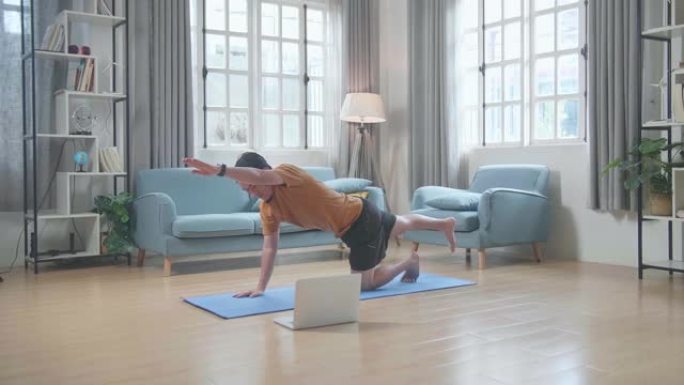 亚洲男子在垫子上，用笔记本电脑在家里摆平衡桌做瑜伽