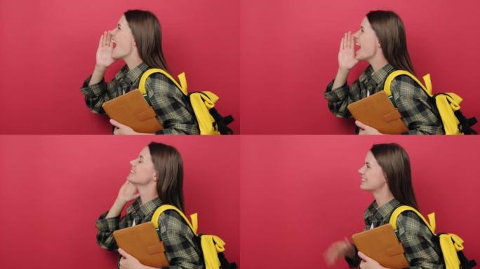20多岁的年轻学生女子肖像，黄色背包拿着两本书向侧面喊着，宣布着什么，在工作室的红色背景墙上孤立地摆