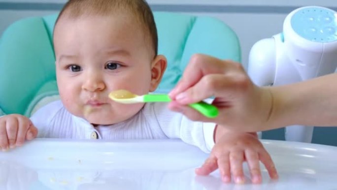 妈妈在孩子们的喂食台上用一勺蔬菜泥喂养婴儿。宝宝食欲，健康营养，辅食介绍。复制空间，模拟