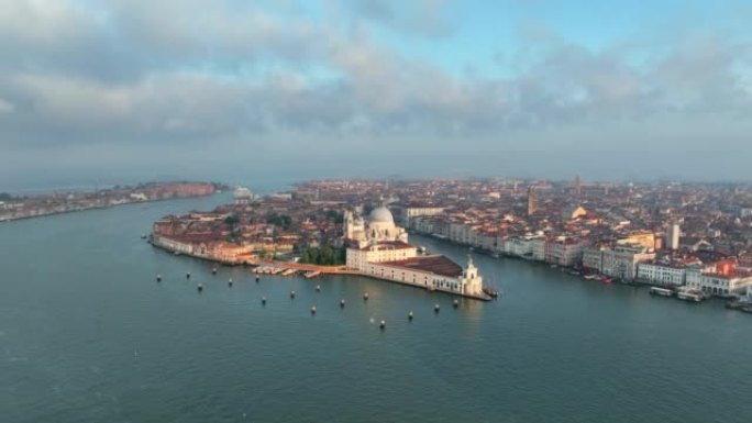 圣玛丽亚德拉致敬罗马天主教堂和小教堂的空中无人机日出场景，大运河和朱德卡运河之间的交通船位于意大利威