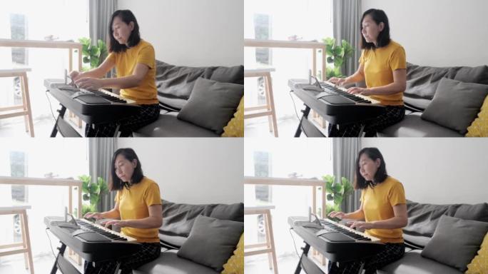 亚洲成年妈妈在家靠窗的沙发上通过移动应用学习弹奏键盘乐器，生活方式概念。