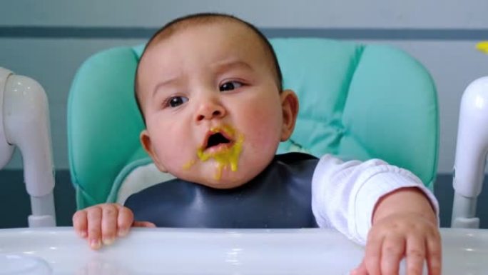 一个饥饿的婴儿用手在高脚椅上的桌子上轻拍，要求吃饭，用勺子轻咬。出牙，异想天开，牙龈发痒，辅食介绍