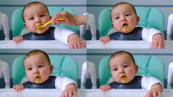 一个饥饿的婴儿用手在高脚椅上的桌子上轻拍，要求吃饭，用勺子轻咬。出牙，异想天开，牙龈发痒，辅食介绍