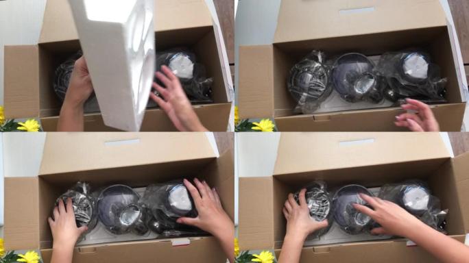 一个女人打开一个装有食品加工机的盒子。他从中取出联合收割机的包装成分，并将其放在桌子上。从上方拍摄，