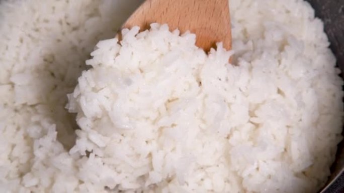用饭勺从锅里舀米饭，用木勺在锅里煮米饭