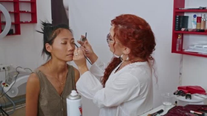 快乐的越南女性造型师和欧洲女性化妆师正在努力为。特写。亚洲女性和造型师的工作。