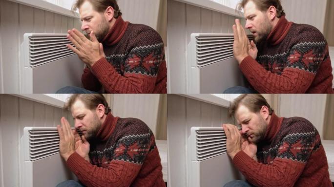 年轻的冻人穿着一件毛衣，冬天的寒冷，脸上带着休克的表情。人正在用电热器呼吸的方式暖手。在家中消磨时间