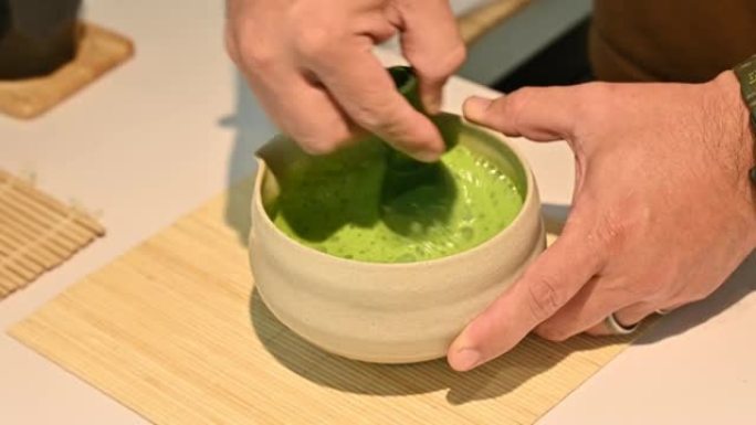 咖啡师使用竹制搅拌器在日本碗中搅拌和混合抹茶粉与水和牛奶。