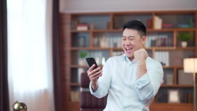 兴奋的亚洲商人拿着智能手机喜出而外的商人工人，员工获胜者庆祝手机在线竞标游戏获胜成功收到读取到的好消