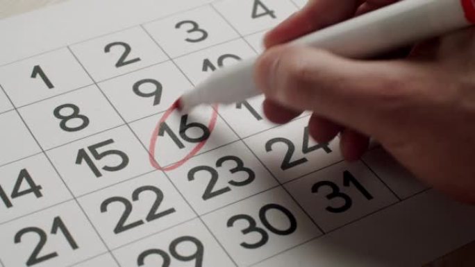 人的手用红笔在纸质日历上写下第16天。