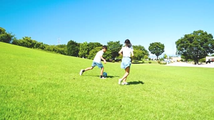 亚洲儿童在蓝天公园踢足球