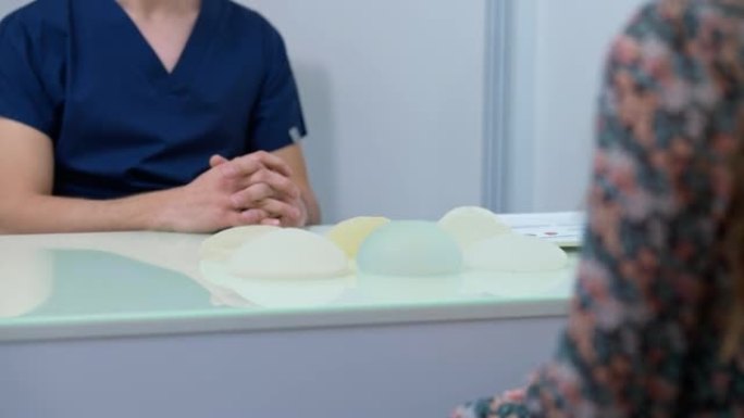 诊所的桌子上有乳房植入物，无法辨认的医生和病人坐在室内握手。中东男人和高加索女人在医院预约握手。