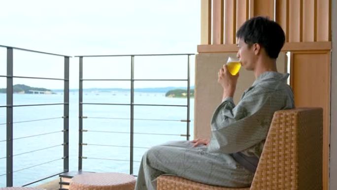 亚洲男子在温泉客栈边看海边喝啤酒