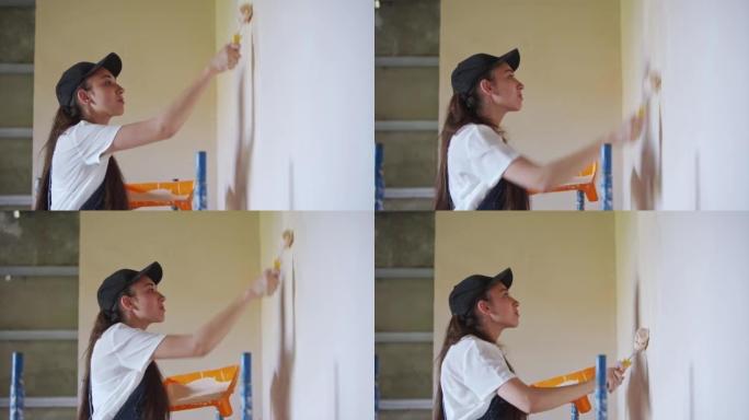 专业画家女性在建筑工地上用滚筒和托盘粉刷墙壁。穿着工作服和帽子的年轻女子在做家居装饰和装修。工人在房