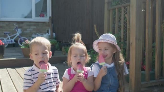 三个可爱的小孩享受美味的冰淇淋蛋卷。吃西瓜冰棒的孩子。儿童兄弟姐妹在家庭花园零食糖果。暑假炎热天气晴