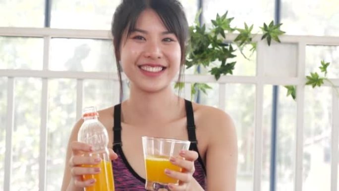 女人双手握着冷橙汁新鲜水果凉饮。亚洲女性微笑笑看相机保健家庭健身生活方式。美丽的女性从鸡尾酒瓶中倒橙
