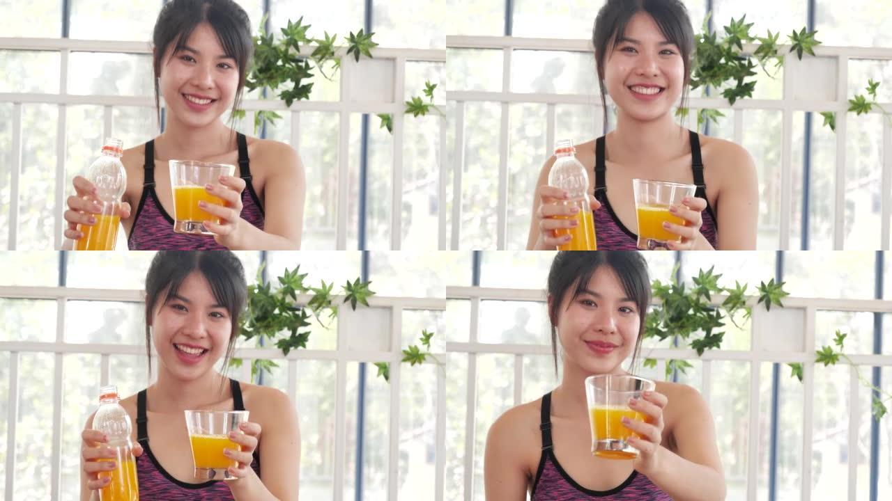 女人双手握着冷橙汁新鲜水果凉饮。亚洲女性微笑笑看相机保健家庭健身生活方式。美丽的女性从鸡尾酒瓶中倒橙