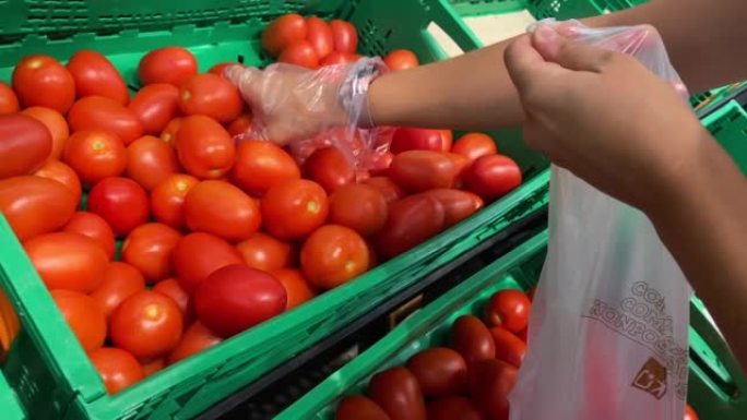 面目全非的女人从绿色超市的篮子里采摘红色西红柿。一个人选择蔬菜放入回收塑料食品袋的视频。