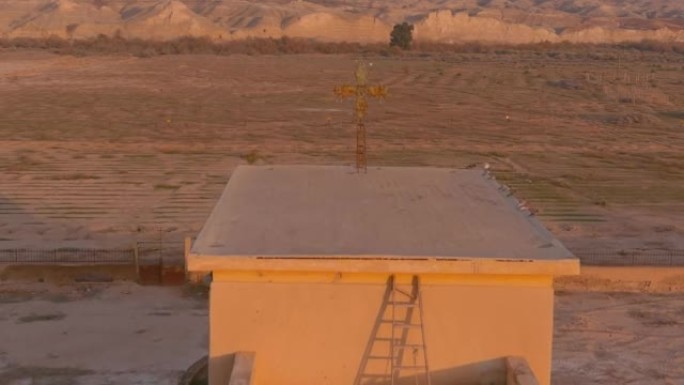 沙漠日落中废弃结构顶部的旧金属十字架，空中