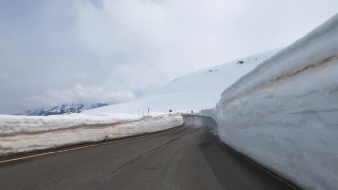 令人眼花Time乱的延时行驶在高阿尔卑斯山的一条潮湿的柏油路上，道路旁的路堤上积雪残存，POV。