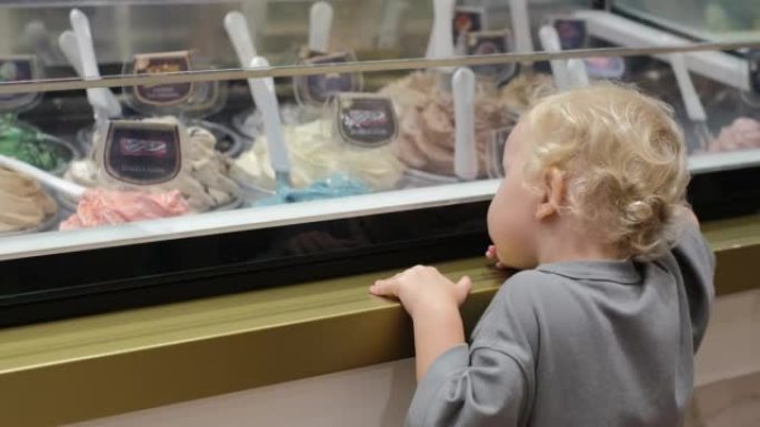 可爱的金发小孩渴望从家庭咖啡馆展示中选择冰淇淋，各种口味。孩子喜欢吃甜食，但不顾后果地吃糖对孩子的牙