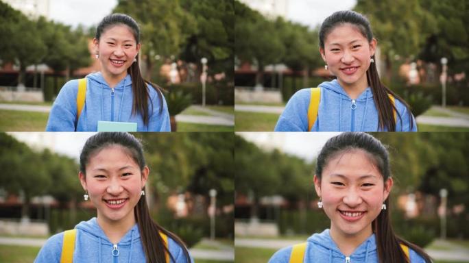 年轻的中国女学生在高中微笑着看着相机。可爱的亚洲女孩在校园里站着大笑的特写肖像。