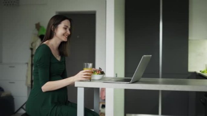 Pregnant woman sitting and eats salad while having